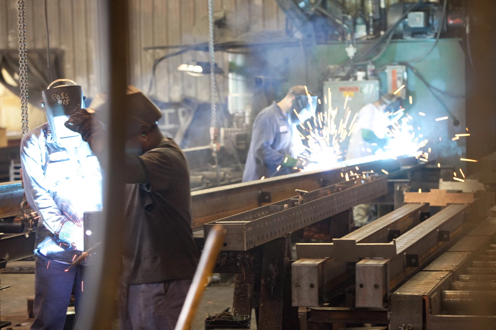 Four Dexco welders working on a piece of metal with sparks flying around them